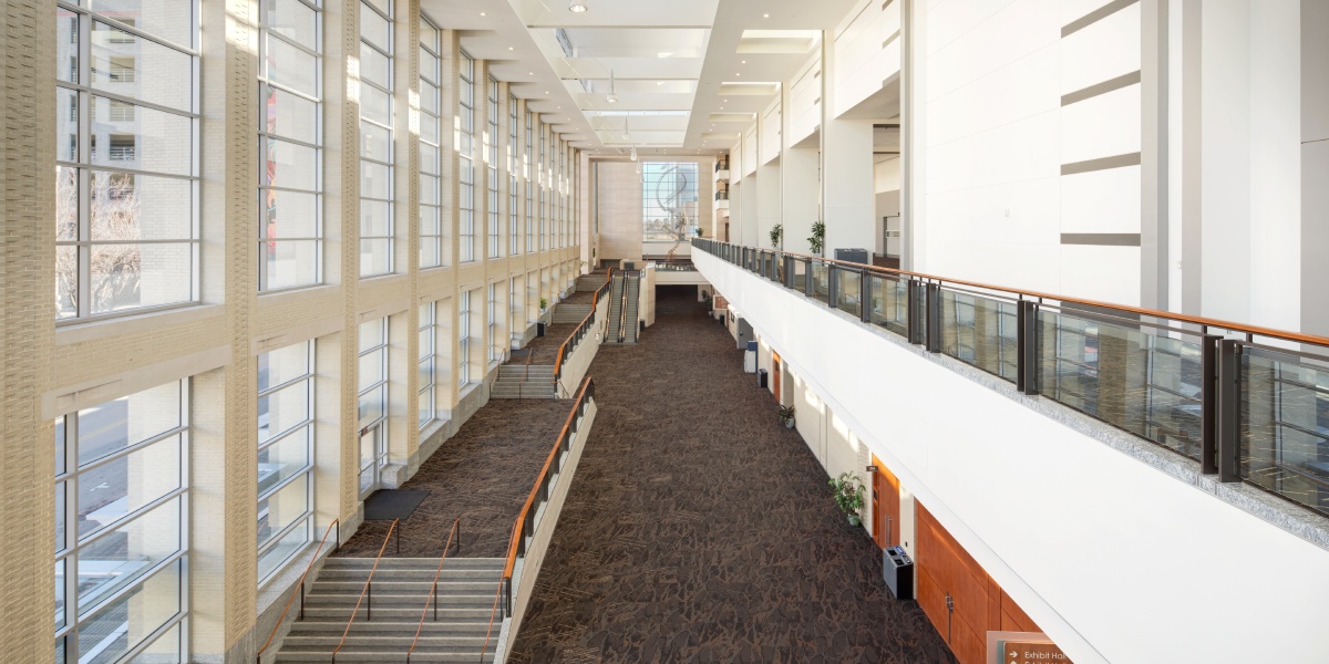 View from above a spacious atrium with floor-to-ceiling windows, modern lighting, neutral tone carpet, and an open mezzanine.